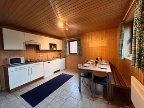 A compact kitchen with white cabinets, a microwave, and a sink. There is a dining table with chairs and a rug on the floor. - Charming Stay by the Meuse (Hastiere)