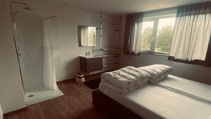 Ein Schlafzimmer mit Bett, Dusche, Waschbecken und einem Fenster mit Vorhängen.