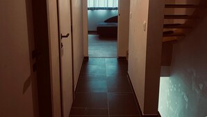 Ein schmaler Korridor mit Fliesenboden, der zu einem Zimmer mit Bett und einem blickdichten Fenster führt.