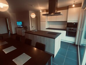 A modern kitchen with a central island, built-in appliances, and a dining area with a dark wooden table and chairs. - Holiday Home in De Panne Near Plopsaland (De Panne)
