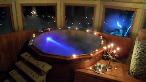 Un bain à remous avec vue sur les lumières de la ville la nuit, des bancs en bois et une table décorative avec des bougies.