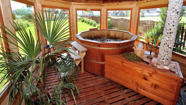 Un belvédère en bois équipé d’un jacuzzi, de bancs en bois et de plantes en pot.