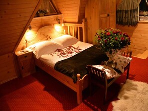 A cozy wooden room with a bed, a nightstand, a chair, and a vase of flowers.