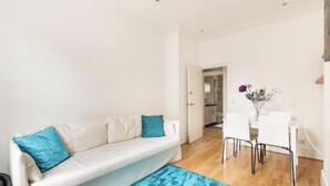 Ein modernes Wohnzimmer mit einem weißen Sofa, Türkis-farbenen Kissen, einem Esstisch mit Stühlen und einer Vase mit Blumen.