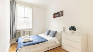 Ein Schlafzimmer mit Bett, Schminktisch, Heizkörper und einem Fenster mit Vorhängen.