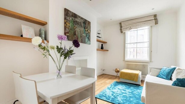 Ein modernes Wohnzimmer mit einem weißen Sofa, einem blauen Teppich mit Muster und einem Gemälde von New York City.
