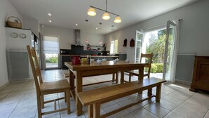 Uma cozinha moderna com uma mesa de jantar de madeira, cadeiras e um banco. Duas luminárias pendentes iluminam a mesa e uma grande janela oferece luz natural.