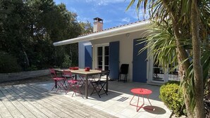 Um pátio com deck de madeira, uma mesa com cadeiras e uma pequena mesa vermelha.