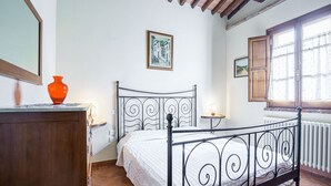 A bedroom with a metal bed frame, a wooden dresser, a vase, and a window with curtains.