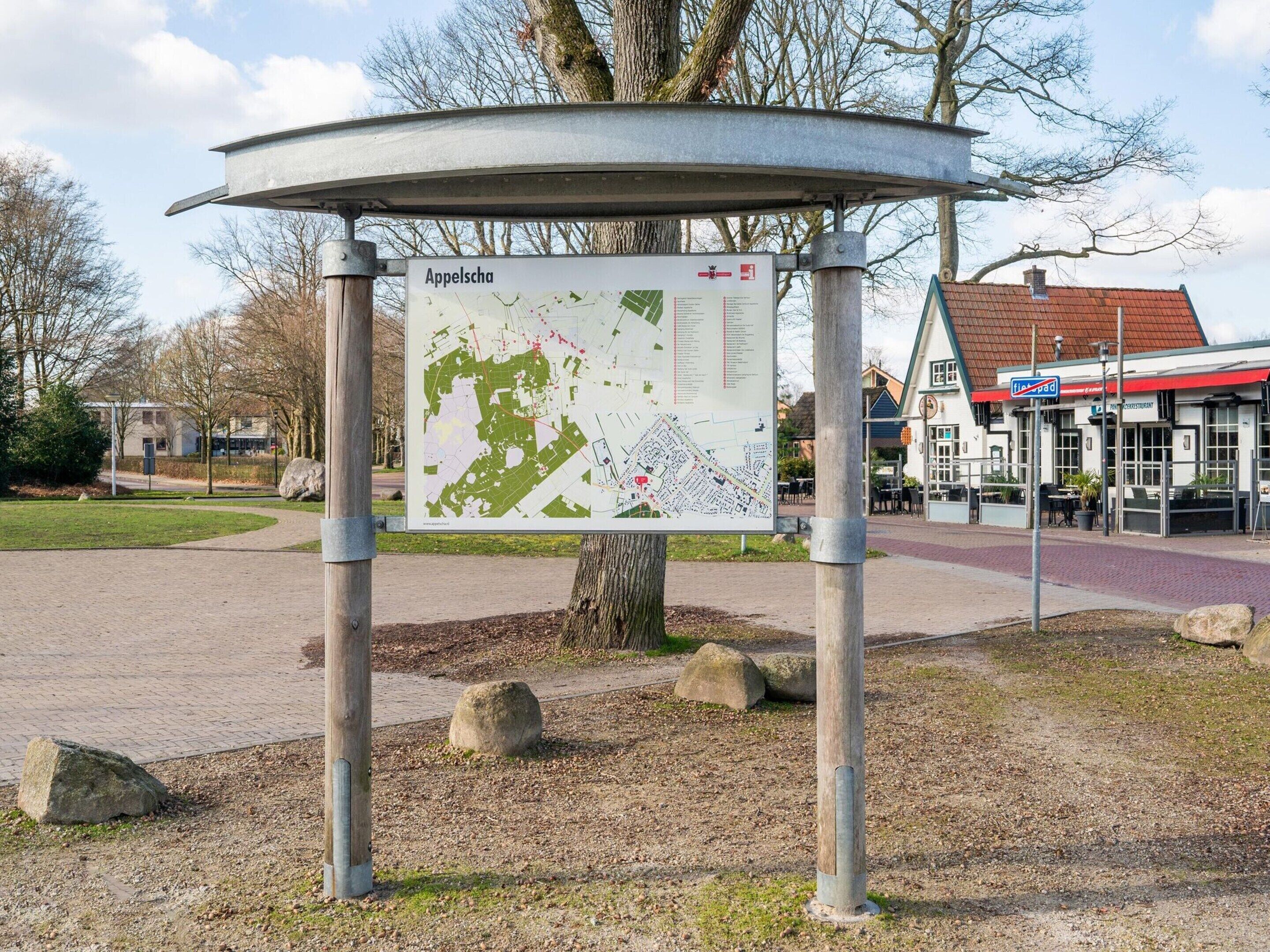 A map sign in a park area with a building in the background.