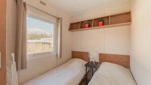 A small, clean room with two single beds, a window with curtains, a shelf with potted plants, and a bedside table with a lamp. - Cosy Holiday Home in Appelscha With Garden (Appelscha)