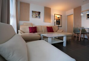 A modern living room with a sofa, a coffee table, and a dining area with chairs. - Familienappartement Marianne mit Pool und Sauna (Freyung)