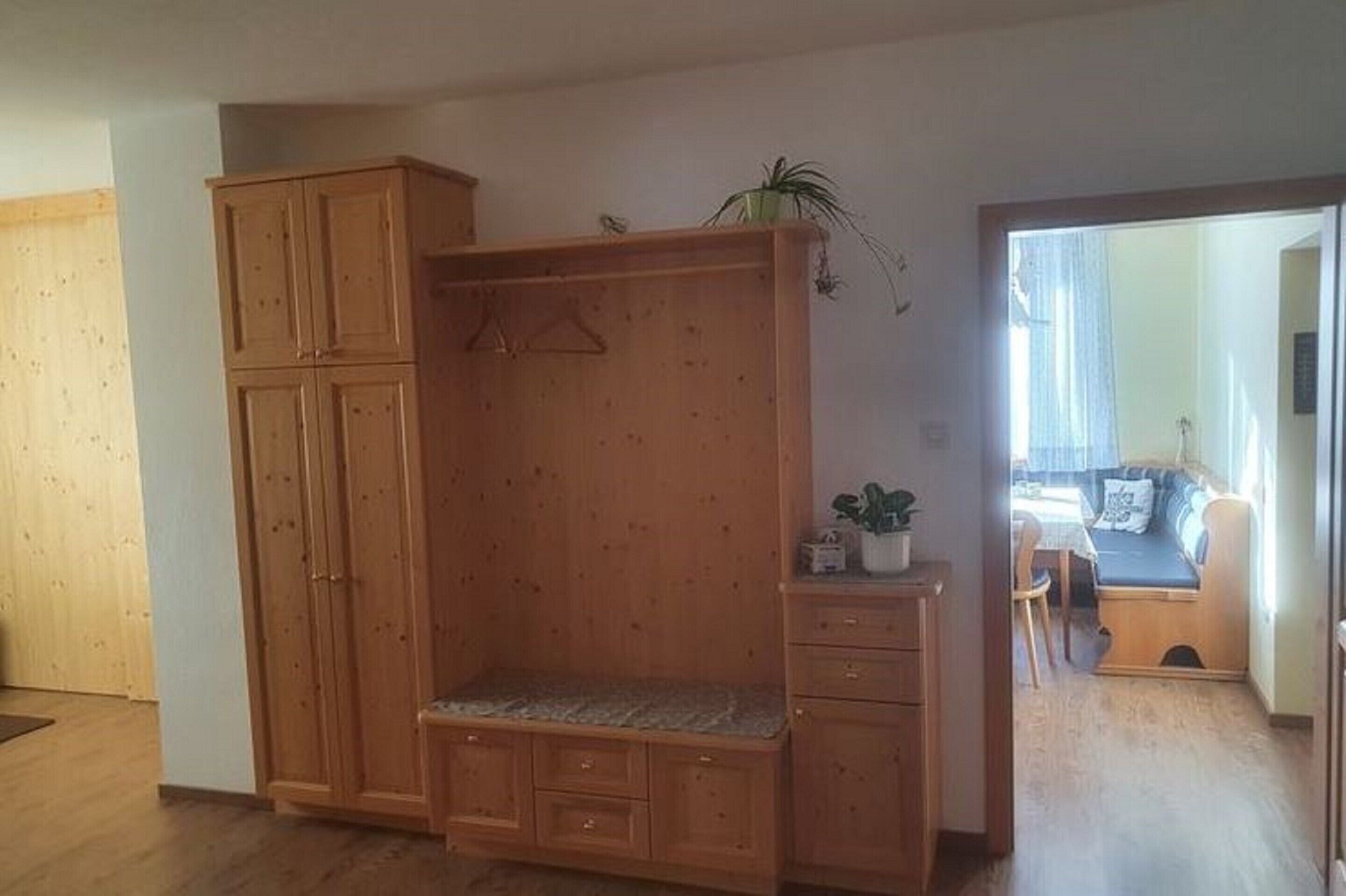 A room with a wooden wardrobe, a bench, and a small table with a plant.