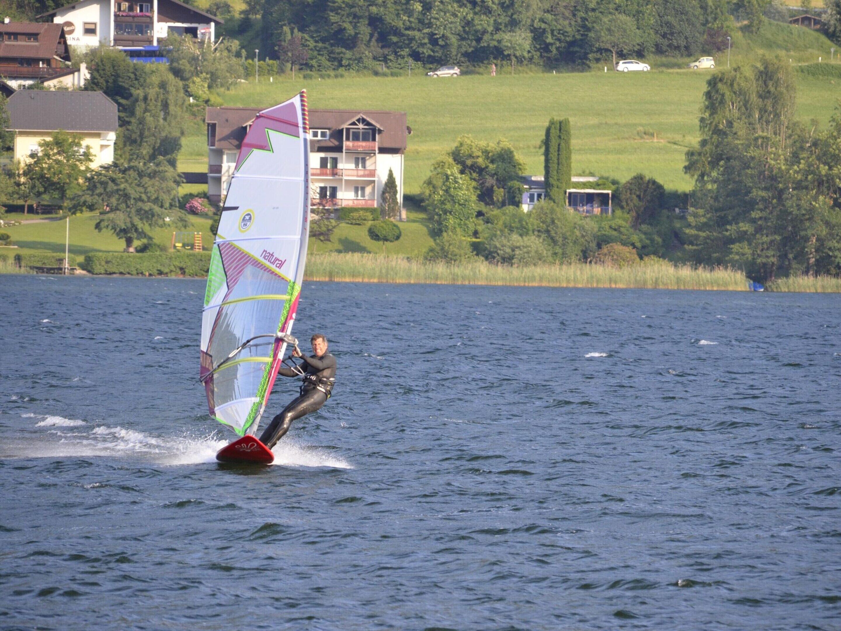 A person windsurfing on a lake with houses in the background.