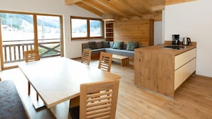 Un interior de madera con una mesa de comedor, sillas, un sofá, una zona de cocina y ventanas amplias que ofrecen vistas al exterior.