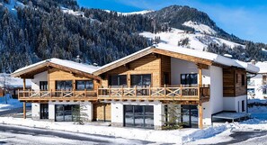Un chalet de dos pisos con fachada de madera, ventanas grandes y un balcón.