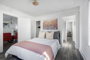 A bedroom with a large bed, a red chair, and a hallway leading to a bathroom.