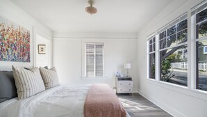Ein Schlafzimmer mit einem großen Bett, einem Nachttisch, einem Fenster mit Jalousien und einem Wandbild.