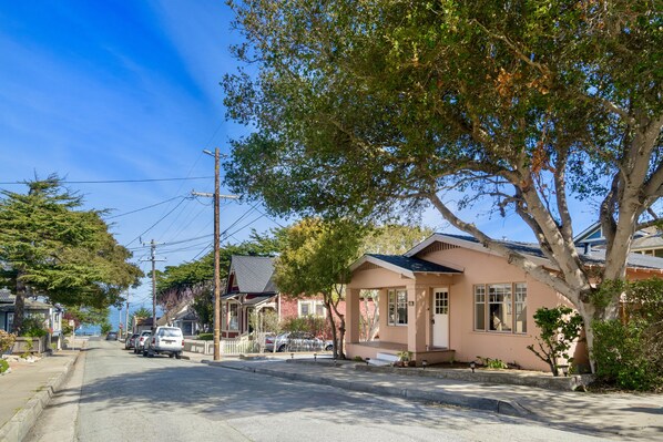 A residential street with houses, a clear sky, and a tree in the foreground.