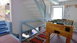 Ein Zimmer mit einem hölzernen Tischkicker, einer Treppe mit blauen Geländern und einem gemusterten Teppich.