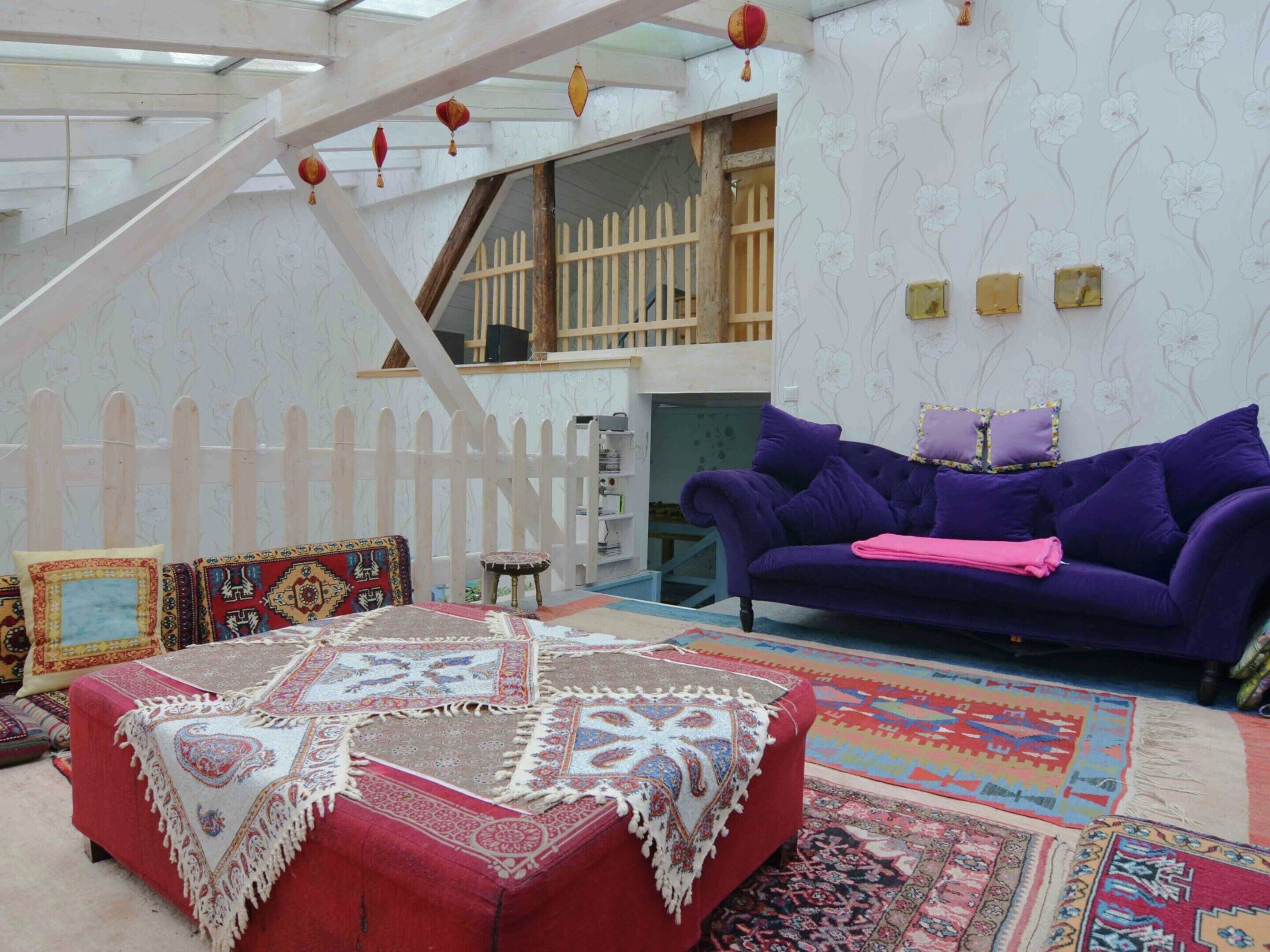 Un salon chaleureux avec un pouf rouge, un canapé violet et une variété de tapis aux couleurs vives.