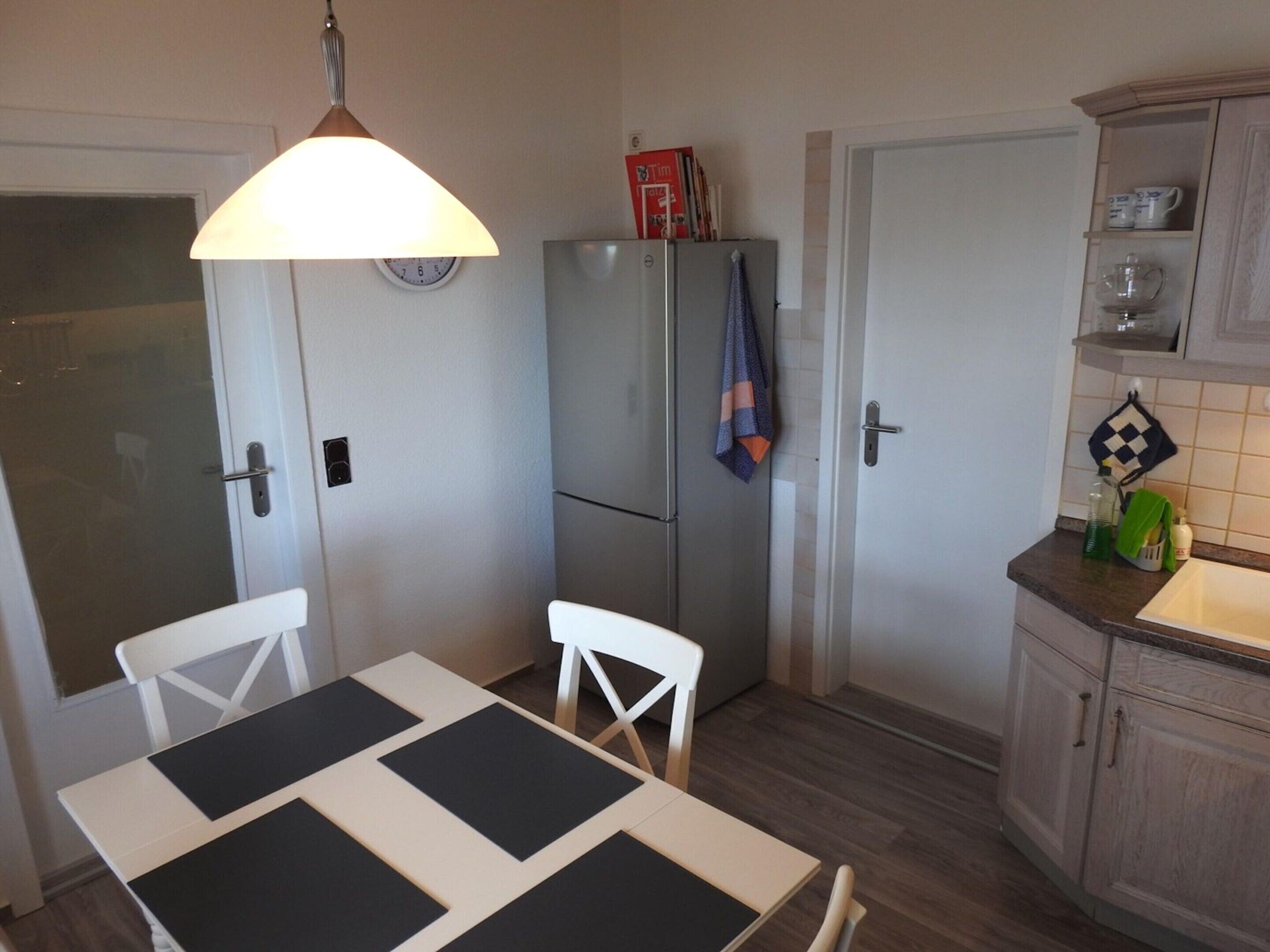 A compact kitchen with a dining table, chairs, a refrigerator, and a hanging light fixture.
