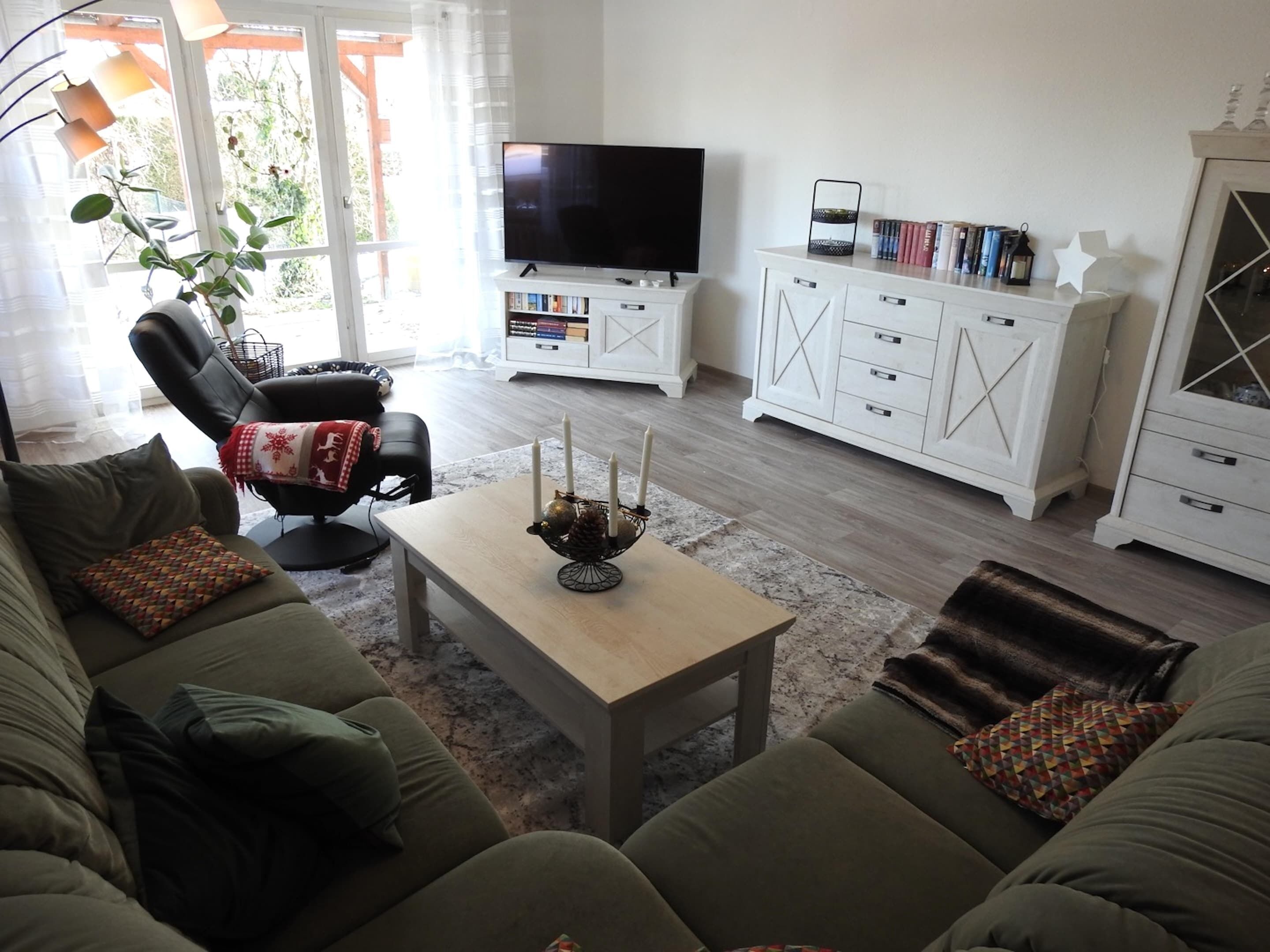 Ein Wohnzimmer mit einer Couch, einem Couchtisch mit Kerzen, einem Fernseher und einem Bücherregal.