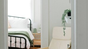 Ein Schlafzimmer mit Bett, Stuhl, Nachttisch und einer hängenden Pflanze.