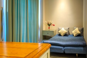 Um quarto com uma cama, uma mesinha de cabeceira, um vaso com flores e uma mesa de madeira.