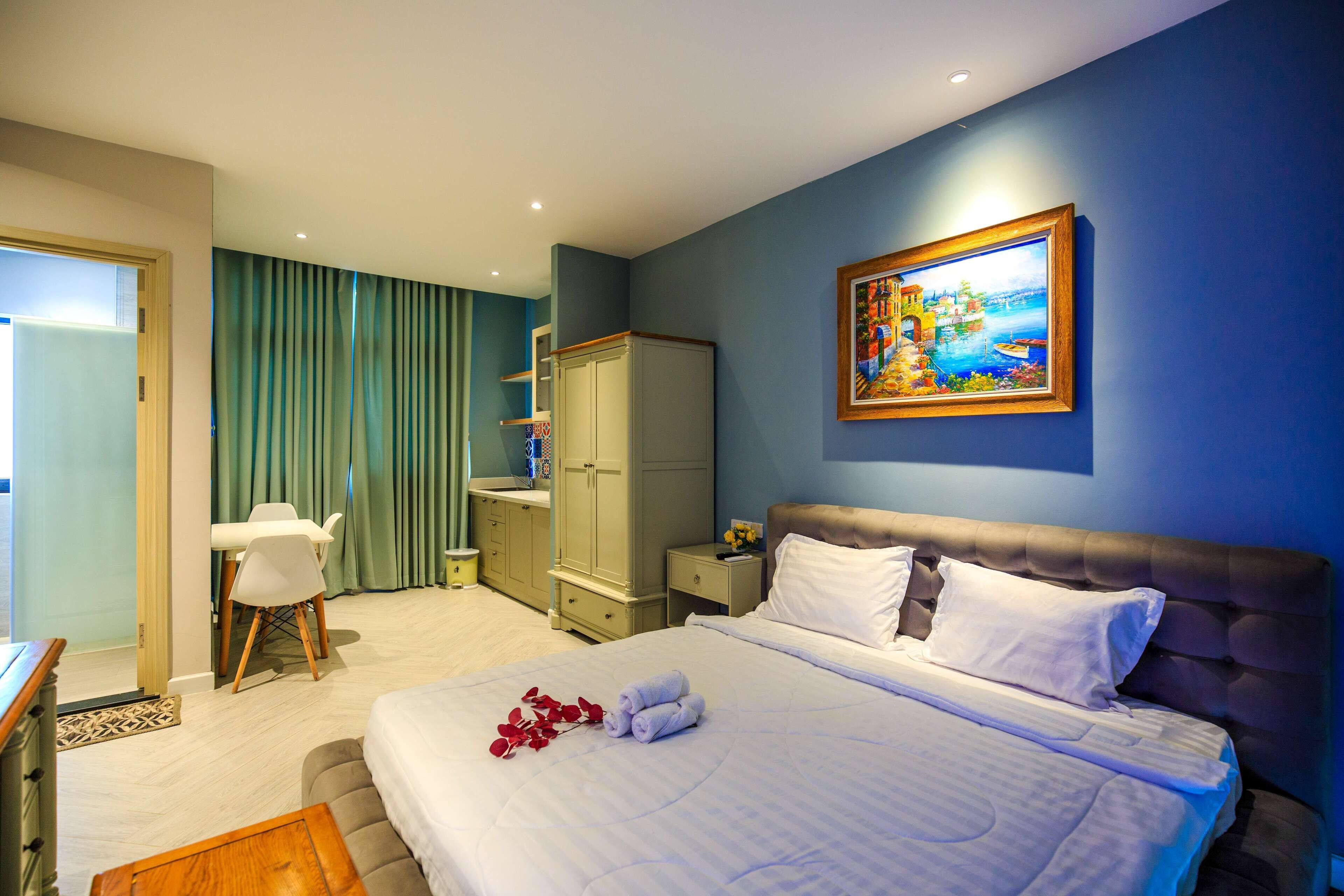 A hotel room with a bed, a painting, a desk, and a chair.