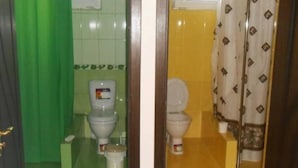 Een badkamer met twee toiletten, waarvan er een een groene gordijn heeft en de ander een patroon.