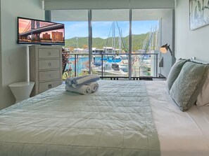 A hotel room with a bed, a TV, a desk, and a view of a marina.