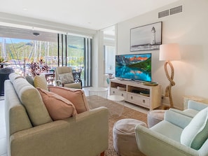 A modern living room with a large TV, comfortable seating, and a view of a marina.
