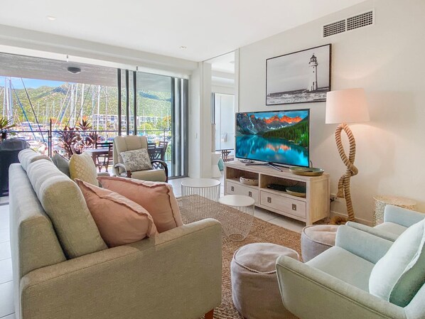 A modern living room with a large TV, comfortable seating, and a view of a marina.