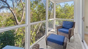 A sunlit room with large windows, wicker furniture, and a view of trees. - Cedars East Getaway–Tennis & Gulf Breezes 507/RVA (Longboat Key)