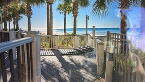 Una terraza de madera con vistas a la playa y palmeras.