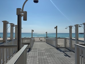 Eine Strandpromenade mit Metallgitterboden, weißen Geländern und freiem Blick auf den Ozean.