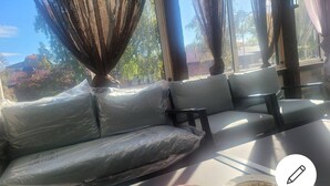 A room with a cushioned bench, a table with a plate of food, and a view of trees and buildings outside. - 2 bed Room Quite and Central House in Orebro (Örebro)