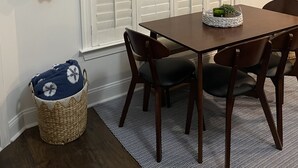 A dining area with a table, chairs, a basket, a hat, and a sign on the wall.