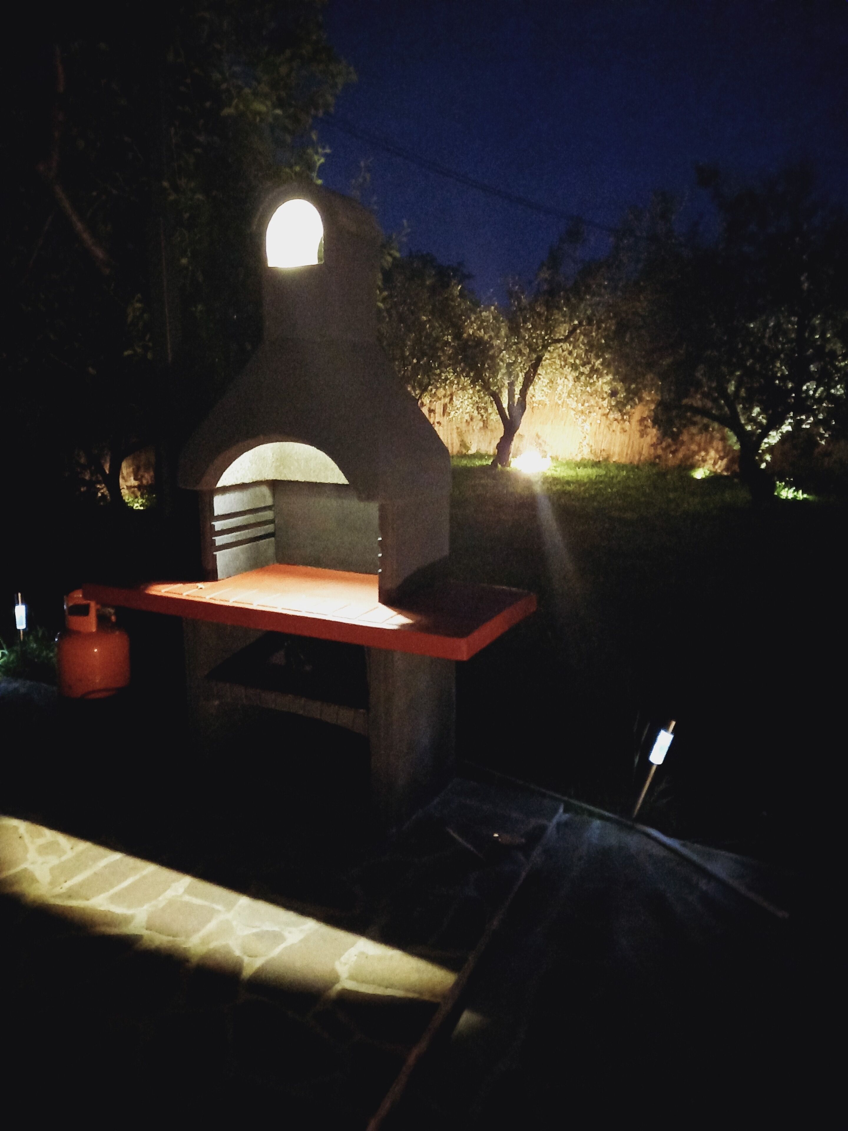 Un horno de ladrillo exterior con chimenea, una encimera roja y un cilindro de gas.
