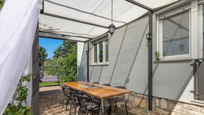An outdoor patio with a wooden table and chairs, a covered area with a white canopy, and a stone floor. - Chill out . (Marcana)