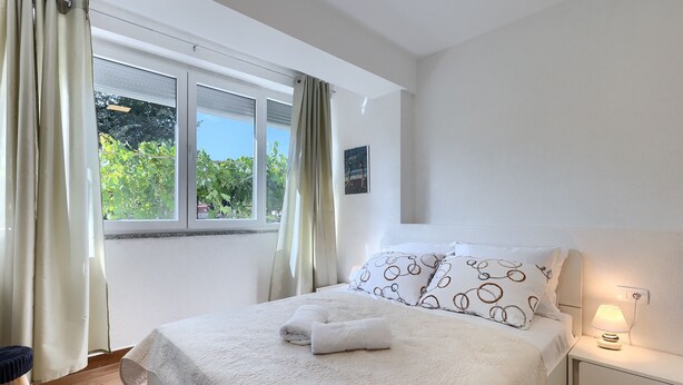 A bedroom with a bed, a nightstand, a lamp, and a window with curtains. - Chill out . (Marcana)