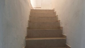 Un escalier recouvert de carreaux beiges, situé dans un couloir étroit aux murs blancs.
