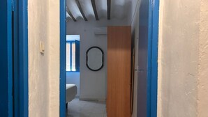 Un couloir étroit aux murs peints en bleu et au sol carrelé. On peut voir une porte en bois et un objet circulaire accroché au mur.