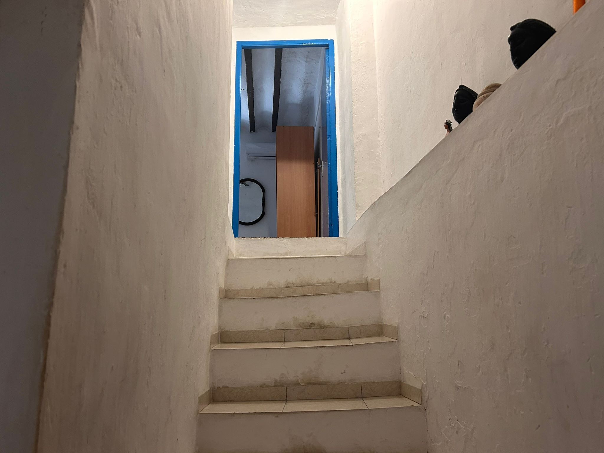En smal trappa med vita väggar och en blå dörr längst upp.