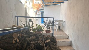 Un étroit couloir extérieur où l’on trouve une pile de bois de chauffage, des plantes en pot et un escalier menant à un niveau supérieur.