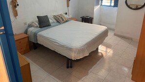 Une chambre à coucher comprenant un lit, des tables de chevet, une fenêtre avec des stores, un miroir et une prise de courant.