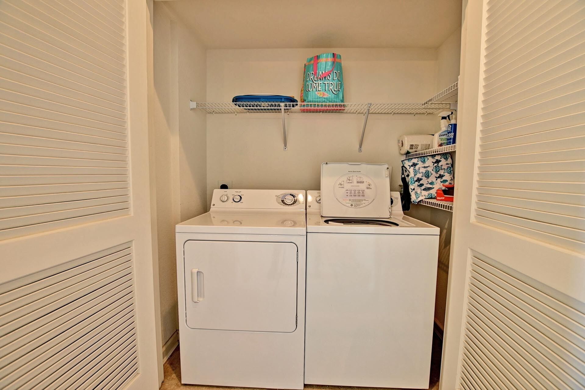 Une buanderie équipée de deux machines à laver et de deux sèche-linge superposés, d’une étagère contenant des produits de lessive et d’une porte dotée d’une poignée.