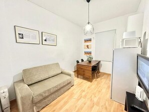 A small, modern room with a sofa, a wooden dining table, a hanging light fixture, and a refrigerator. - Madrid Rio Antonio López 1 (Madrid)