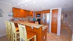 A kitchen with wooden cabinets, a stainless steel refrigerator, and a granite countertop.